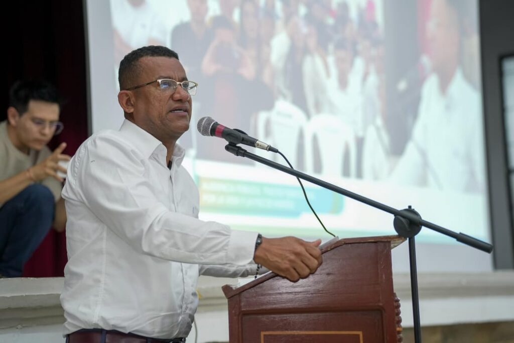 El Gobernador de Nariño, Luis Alfonso Escobar Jaramillo, interviene desde un podio de madera durante la audiencia pública en Sandoná sobre el Pacto Territorial. De fondo se observa una pantalla de proyección con la imagen del público asistente.