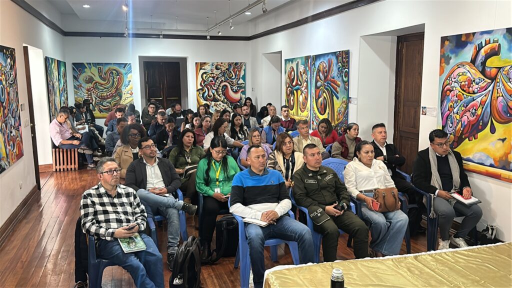 Reunión presencial en un salón concurrido con obras de arte en las paredes, donde asistentes escuchan atentamente la reactivación del Consejo Departamental de Reincorporación en Nariño.