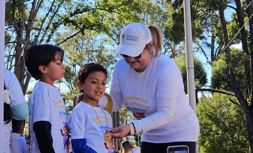 La Secretaria de Equidad de Género e Inclusión Social de Nariño, Liliana Montúfar, entrega una medalla a un niño en la carrera "Al ritmo de mi voz".