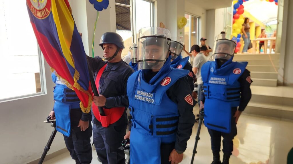 Integrantes de la Brigada de Desminado Humanitario del Ejército Nacional durante el acto oficial en San Pablo, portando uniformes de protección azules y sosteniendo la bandera de Colombia.