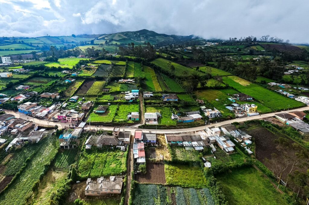 Vista aérea del resguardo indígena en Túquerres, Nariño, que muestra la nueva infraestructura de placa huella atravesando un paisaje rural de minifundios y zonas de cultivo. Se observa la vía pavimentada que conecta diversas viviendas y parcelas agrícolas bajo un cielo nublado.