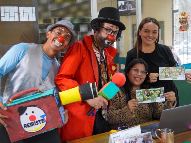 Dos hombres vestidos de payasos junto a dos mujeres que sostienen billetes del Segundo Sorteo Extraordinario de la Lotería de Nariño en una oficina.
