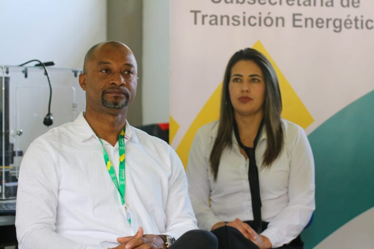 El Subsecretario de Transición Energética de Nariño, Gerson Preciado, hombre afrodescendiente con camisa blanca y escarapela institucional verde, se encuentra sentado junto a una colaboradora. Al fondo, se observa parcialmente un pendón que dice Subsecretaría de Transición Energética.