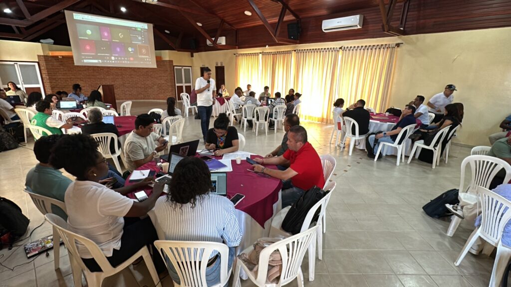 El Secretario de Paz de Nariño, Alex Javier González, se dirige a los asistentes durante el Comité Ordinario de Justicia Transicional en Tumaco. Se observan mesas de trabajo con funcionarios y líderes de víctimas utilizando computadores y documentos para la aprobación de los Planes Operativos Anuales de atención y protección.