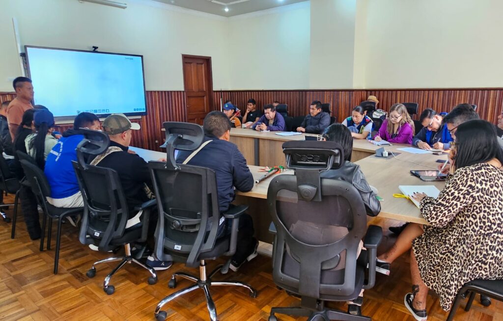 Mesa de trabajo y diálogo social entre el equipo técnico de la Gobernación de Nariño y líderes de las comunidades indígenas Awá, Telembí y El Sande en una sala de reuniones con una pantalla digital.