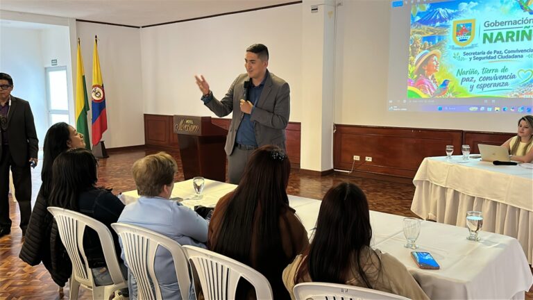 El secretario de Paz y Derechos Humanos, Alex Javier González, habla por micrófono ante los asistentes del diplomado junto a una proyección institucional de la Gobernación de Nariño.