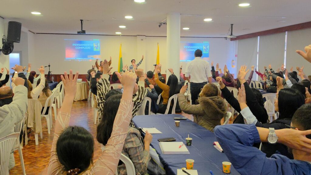 Asistentes al taller pedagógico levantan las manos durante una actividad dinámica sobre pensamiento complejo y educación emocional.