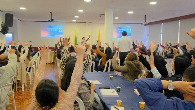 Asistentes al taller pedagógico levantan las manos durante una actividad dinámica sobre pensamiento complejo y educación emocional.
