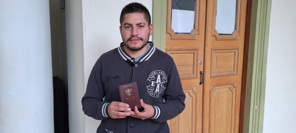 Jaider Paredes, ciudadano del municipio de Yacuanquer, sostiene y muestra el nuevo pasaporte colombiano con diseño de alta seguridad frente a una puerta de madera en la Gobernación de Nariño.