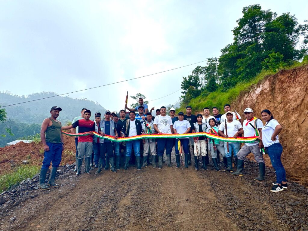 Integrantes de la comunidad indígena Awá del Resguardo Planadas Telembí y operarios sostienen una cinta tricolor durante la entrega de 2,6 kilómetros de vía mejorada en zona rural de Samaniego, Nariño.