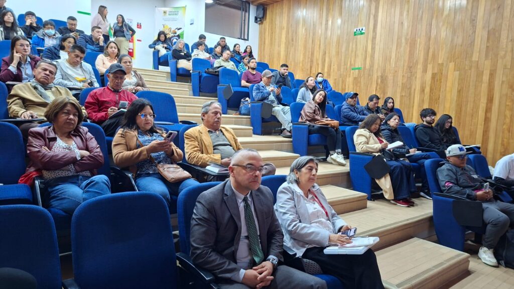 Auditorio lleno con personas atentas en las bancas azules escuchando una capacitación.Título: Asistentes en Auditorio para Capacitación.