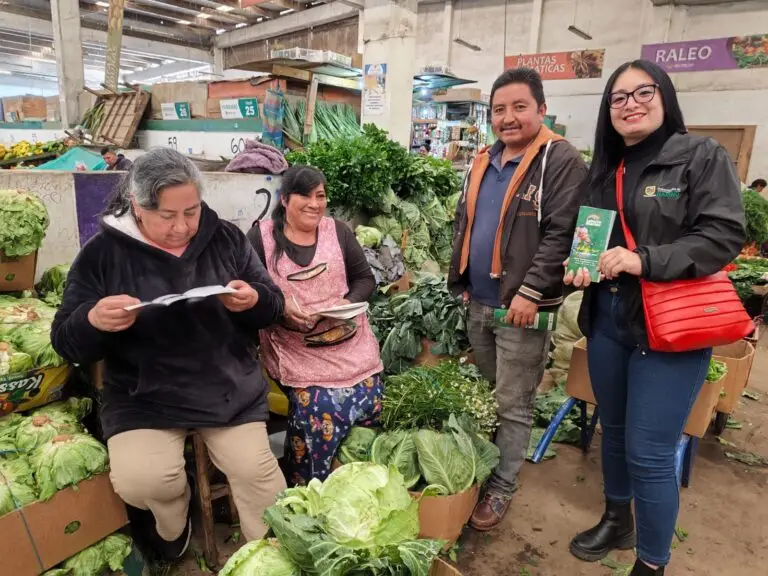 Una funcionaria de la Gobernación de Nariño entrega folletos informativos de la campaña "Juega Legal" de la Lotería de Nariño a vendedores de verduras en una plaza de mercado.