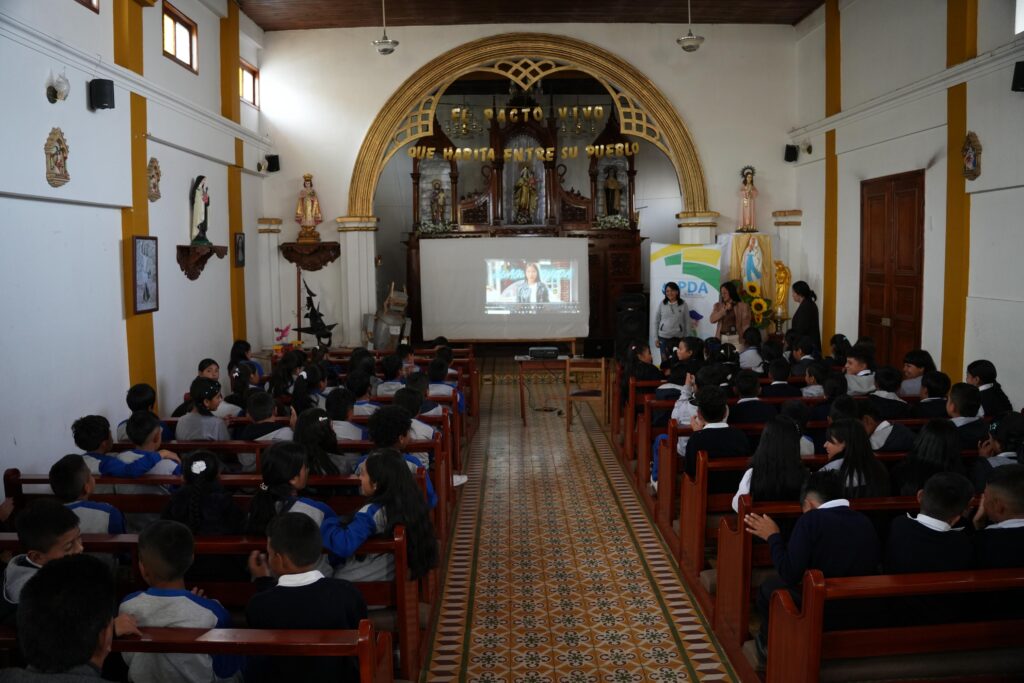 Estudiantes escolares sentados en las bancas de una capilla o salón parroquial atendiendo a una proyección audiovisual sobre el cuidado del agua organizada por el PDA Nariño