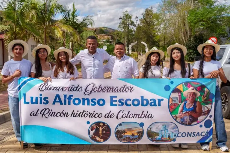 El Gobernador de Nariño, Luis Alfonso Escobar, y el Alcalde de Consacá, Weykman Jojoa, posan sonrientes junto a un grupo de jóvenes locales que sostienen una pancarta de bienvenida con fotos y el texto "Bienvenidos al Rincón Histórico de Colombia Consacá", durante una visita institucional.