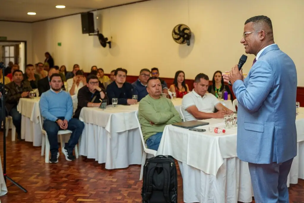 Vista de perfil del Gobernador Luis Alfonso Escobar Jaramillo dirigiéndose a un salón lleno de alcaldes, alcaldesas y delegados de Nariño, quienes se encuentran sentados en mesas con manteles blancos atendiendo la sesión de trabajo.