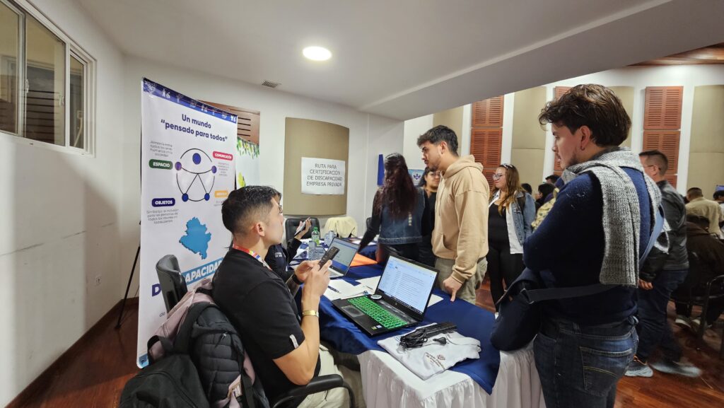 Stand informativo con un pendón titulado "Un mundo pensado para todos" y personal atendiendo a jóvenes en la Feria de Inclusión Laboral de Nariño.