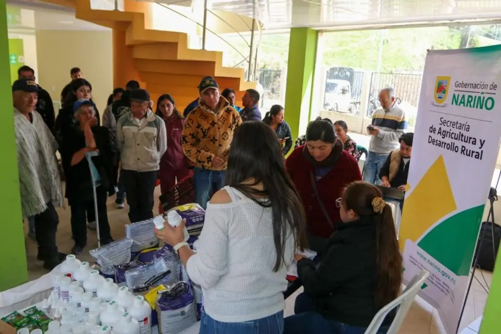 Funcionarias de la Secretaría de Agricultura y Desarrollo Rural de Nariño entregan kits veterinarios e insumos agropecuarios a comuneros del Resguardo Indígena de Iles. A un costado se observa el pendón institucional de la Gobernación.