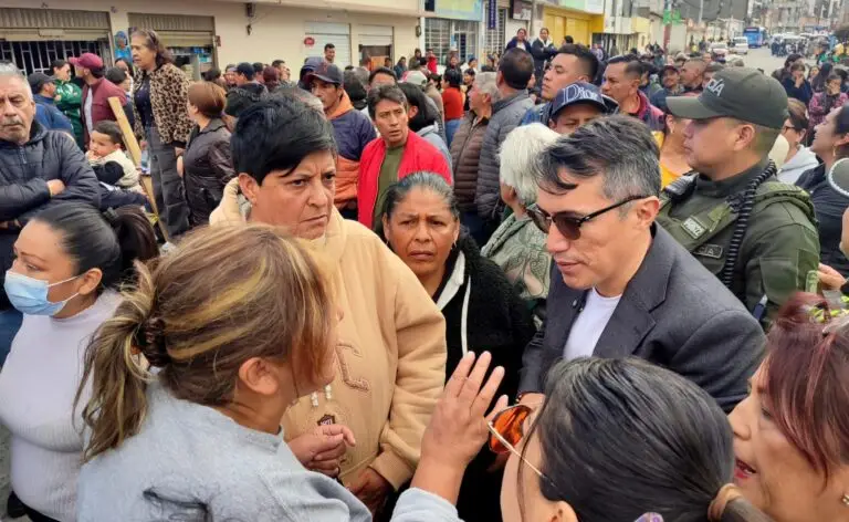 Fotografía en primer plano que muestra al Secretario de Gobierno de Nariño, Fredy Gámez, dialogando directamente con una mujer de la comunidad de Ipiales durante una manifestación por la crisis del agua. Gámez, de gafas de sol y chaqueta gris, escucha atentamente a la mujer, quien gesticula con la mano mientras se dirige a él. Alrededor, otras personas y un policía observan la escena en una calle concurrida.