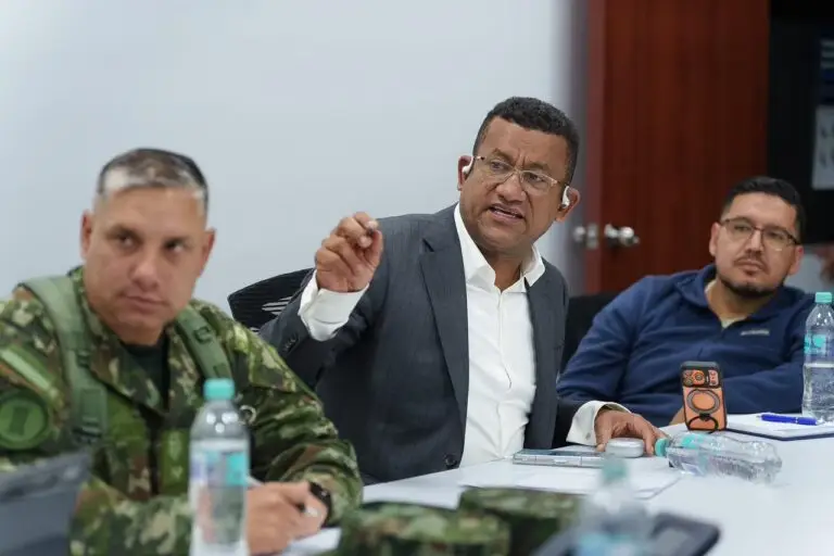 El Gobernador de Nariño, Luis Alfonso Escobar Jaramillo, habla firmemente sosteniendo un bolígrafo en su mano derecha durante la sesión del PMU, flanqueado por un oficial militar y un asistente civil.