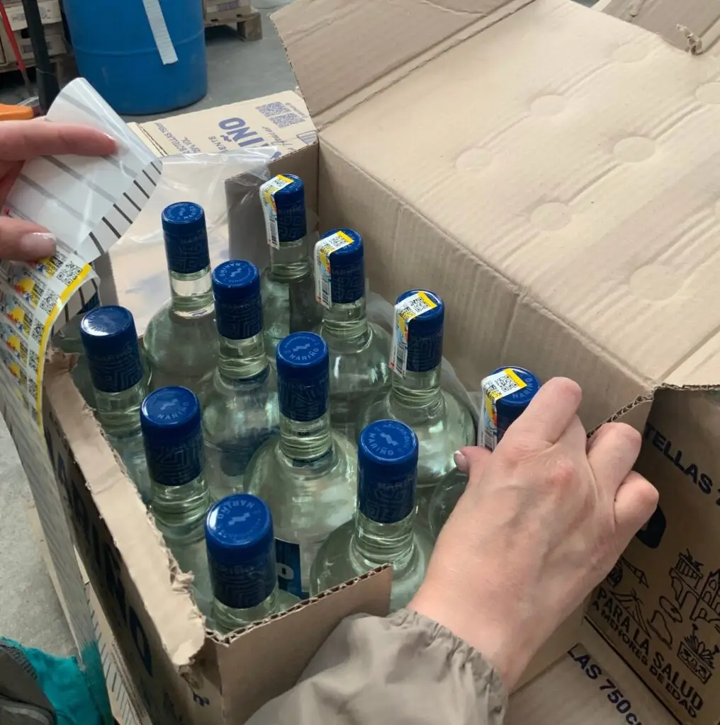 Inspección y colocación de estampillas de control en botellas de Aguardiente Nariño dentro de una caja de cartón.