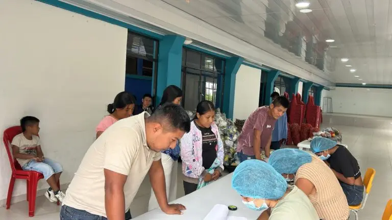 Proceso de registro de padres de familia para recibir las canastas alimentarias del PAE en Nariño. Se observa al personal técnico con gorros y tapabocas atendiendo a los acudientes sobre una mesa blanca.