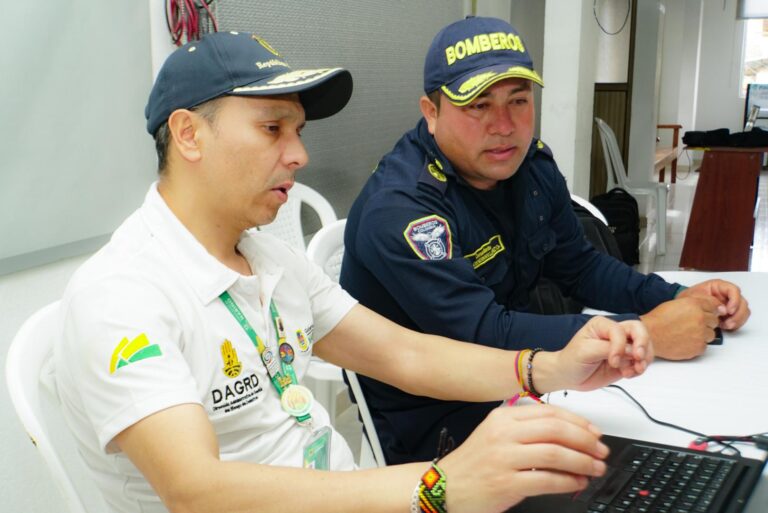 Funcionario de la Dirección Administrativa de Gestión del Riesgo de Desastres (DAGRD) y oficial de Bomberos coordinan acciones operativas frente a un computador portátil.