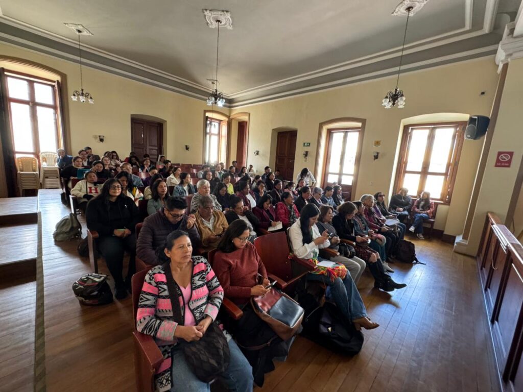 Vista general de un auditorio con piso de madera e iluminación natural donde un grupo numeroso de mujeres, organizaciones y lideresas sociales asisten sentadas en hileras de sillas a una jornada de rendición de cuentas sobre participación ciudadana.