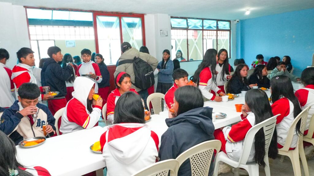 Estudiantes vestidos con uniforme escolar deportivo blanco y rojo consumen complementos alimenticios en el comedor de una institución educativa de Nariño.