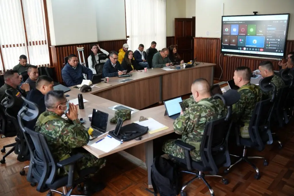 Autoridades militares, de policía y civiles reunidos en una mesa en U durante el Consejo Extraordinario de Seguridad de Nariño, observando una gran pantalla con la videollamada de los alcaldes.