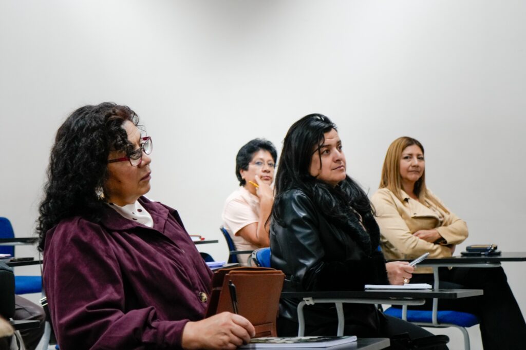 Cuatro mujeres prestadoras de servicios turísticos de Nariño sentadas en pupitres individuales, prestando atención y tomando notas durante el curso de educación financiera.