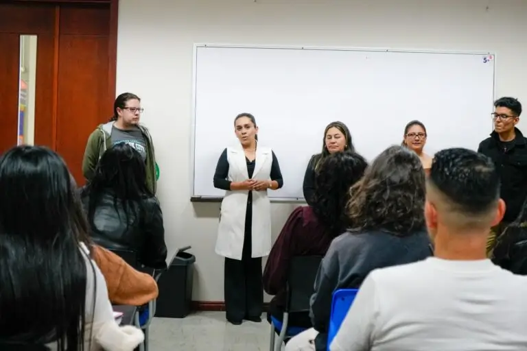 Una facilitadora de pie frente a un tablero blanco de la Universidad CESMAG expone ante el grupo de prestadores turísticos de Nariño sentados en sus pupitres.
