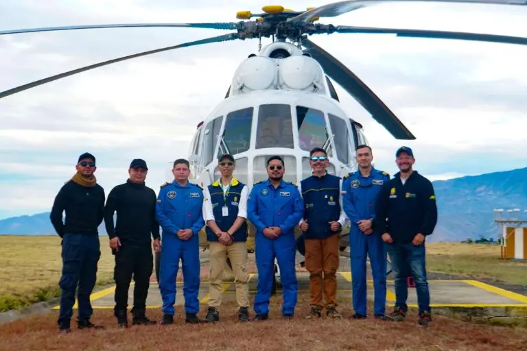 Fotografía de grupo de ocho hombres, incluyendo personal de la Gobernación de Nariño y pilotos de aviación, frente a un helicóptero blanco en un helipuerto de montaña con cielo nublado.