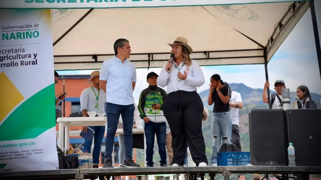 Una mujer con micrófono dirigiéndose al público junto a un funcionario en la tarima oficial de la Gobernación de Nariño durante la Subregional de La Mejor Taza Nariño 2026 en La Unión.