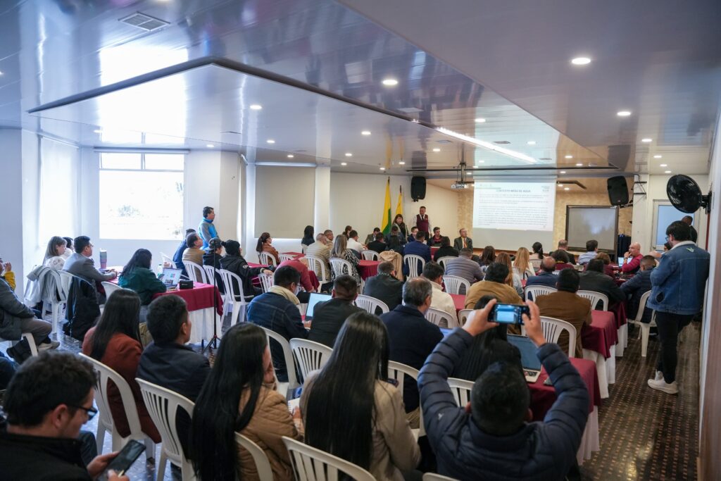 Vista general de la mesa de trabajo interinstitucional del COTSA sobre la Gobernanza del Agua en Ipiales, con asistentes reunidos en un salón de eventos.  