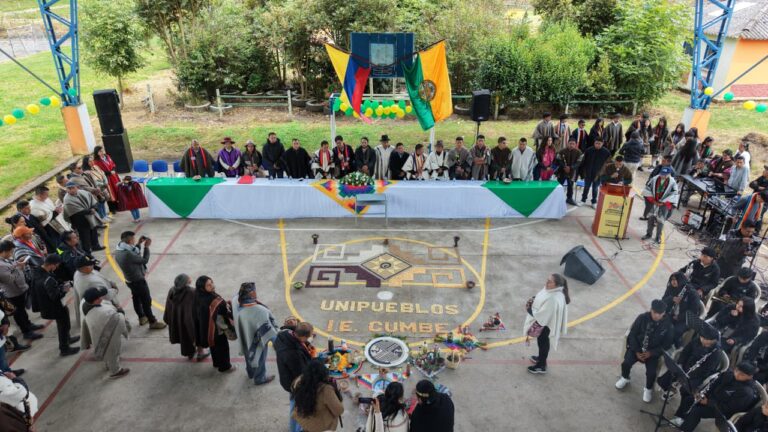 El viceministro de Educación Superior, Ricardo Moreno Patiño, posa al aire libre junto a líderes indígenas con ruana y sombrero, mujeres y niños escolares en uniforme que sostienen pequeñas banderas de Nariño.