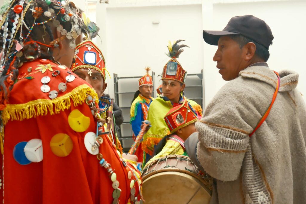 Integrantes de los Danzantes de Males luciendo vestuarios tradicionales decorados con espejos y cintas en diálogo con un habitante local.  