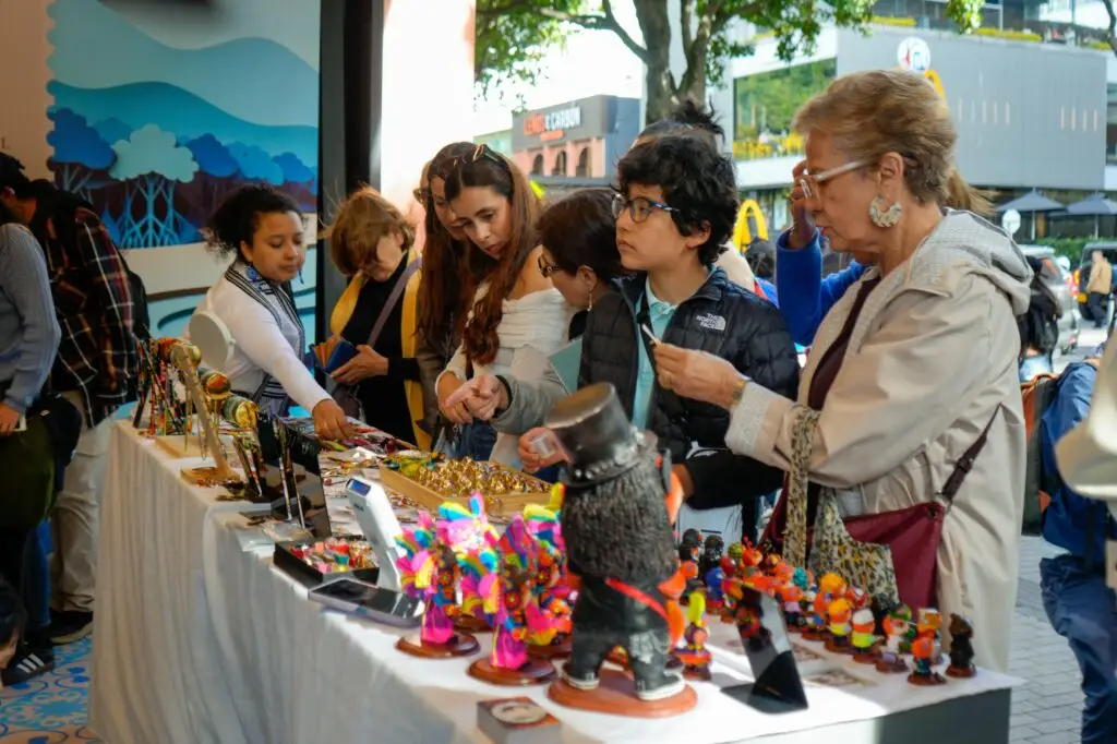 Visitantes observando y comprando artesanías, joyería y figuras tradicionales de Nariño en un estand del Parque de la 93 en Bogotá.