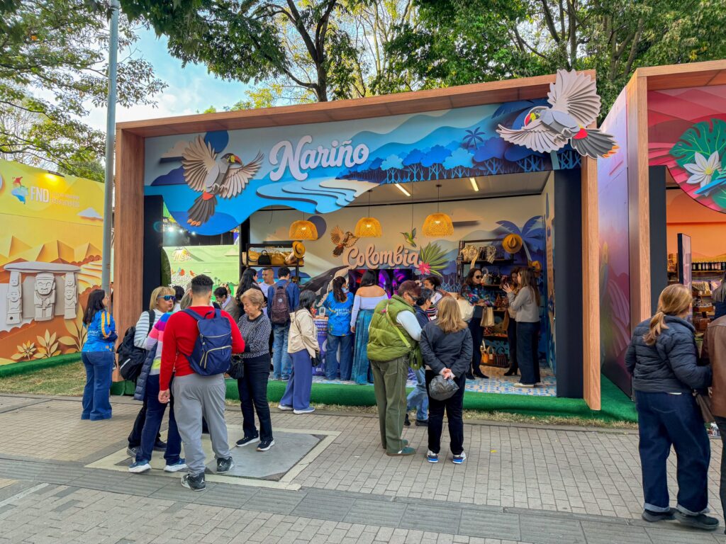 Estand institucional del departamento de Nariño decorado con aves representativas y paisajes, concurrido por visitantes durante una feria turística en Bogotá.