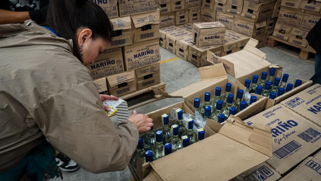 Funcionaria realizando el conteo e inspección de botellas de Aguardiente Nariño dentro de cajas abiertas en bodega.