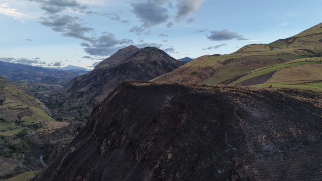 Vista panorámica aérea de una ladera montañosa en Nariño con grandes extensiones de capa vegetal carbonizada por el fuego, junto a terrenos agrícolas verdes bajo un cielo nublado.  