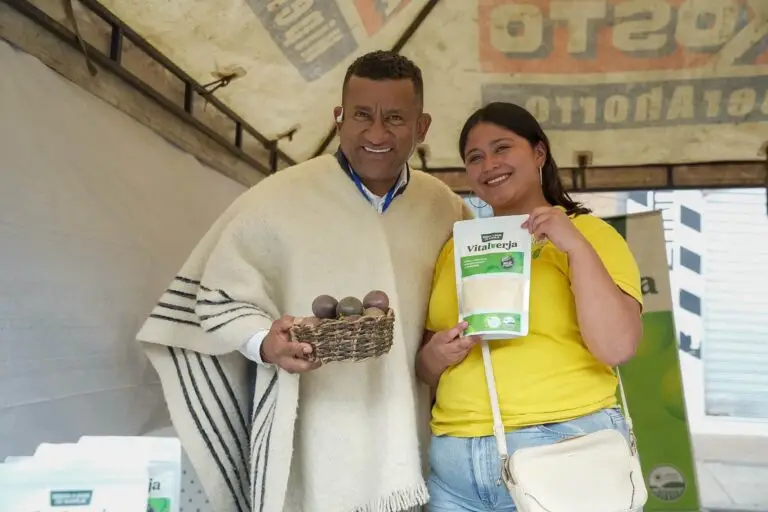 El gobernador Luis Alfonso Escobar vistiendo una ruana blanca junto a una emprendedora que muestra un producto empacado en la feria de Túquerres.