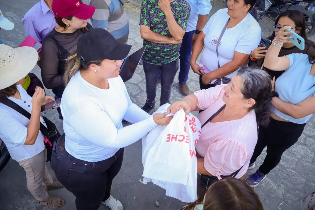Una joven con gorra negra y camiseta blanca entrega un paquete de ayuda a una mujer mayor con blusa rosada durante la jornada en Ancuya.