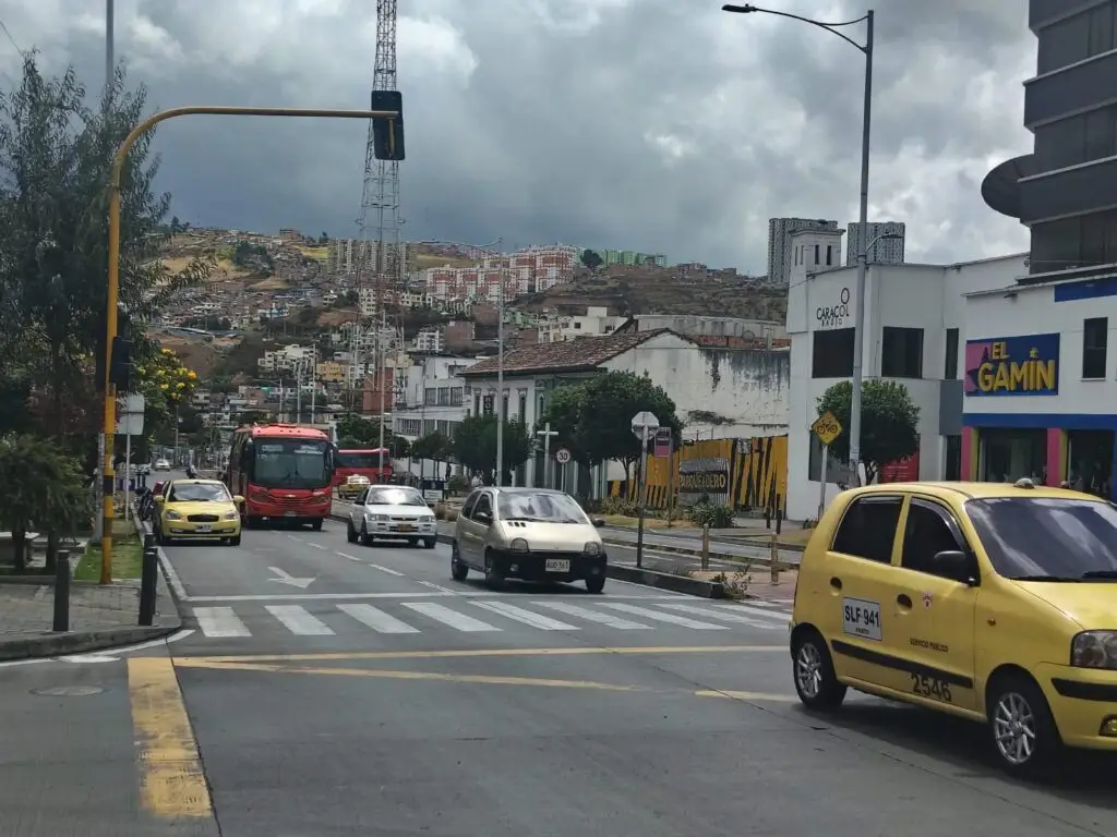 Flujo vehicular de taxis, automóviles particulares y transporte público transitando por una avenida urbana en Pasto, Nariño.