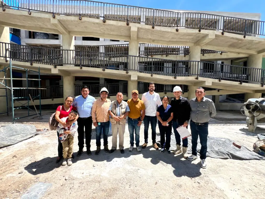 Un grupo de diez personas, entre las que se incluyen funcionarios con casco de obra, adultos de la comunidad y un niño, posan frente a un sistema de rampas de concreto de la edificación en construcción.