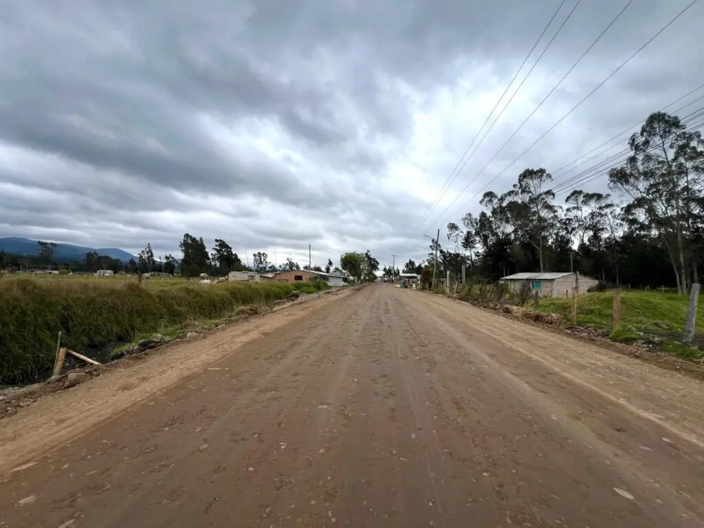 Vista de un corredor vial en tierra, rodeado de pastizales y algunas viviendas rurales, que corresponde al tramo de acceso al casco urbano de Cumbal bajo un cielo nublado.