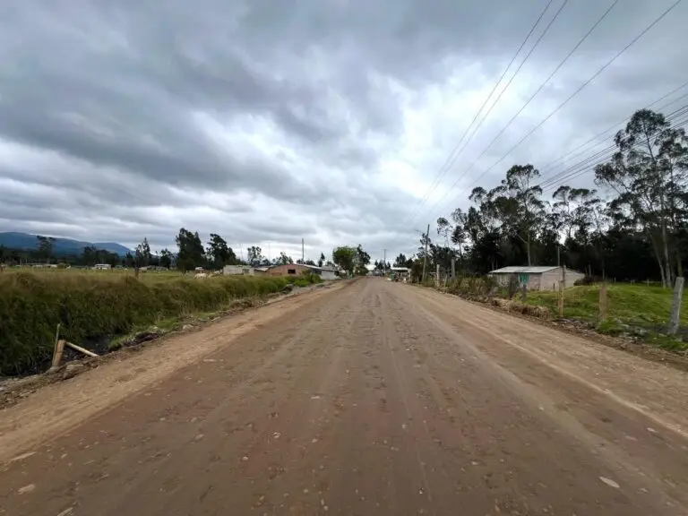 Vista de un corredor vial en tierra, rodeado de pastizales y algunas viviendas rurales, que corresponde al tramo de acceso al casco urbano de Cumbal bajo un cielo nublado.