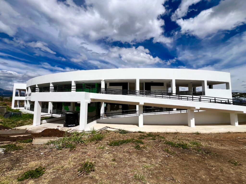 Vista exterior de la renovada fachada blanca y curva de la Ciudadela Educativa de Chachagüí, destacando una amplia rampa de acceso peatonal bajo un cielo azul con nubes.