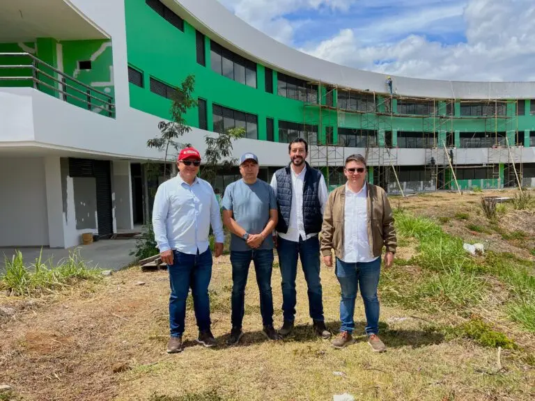 Cuatro hombres posando frente a la edificación en construcción de la Ciudadela Educativa de Chachagüí, la cual presenta una fachada curva en colores verde y blanco con andamios.