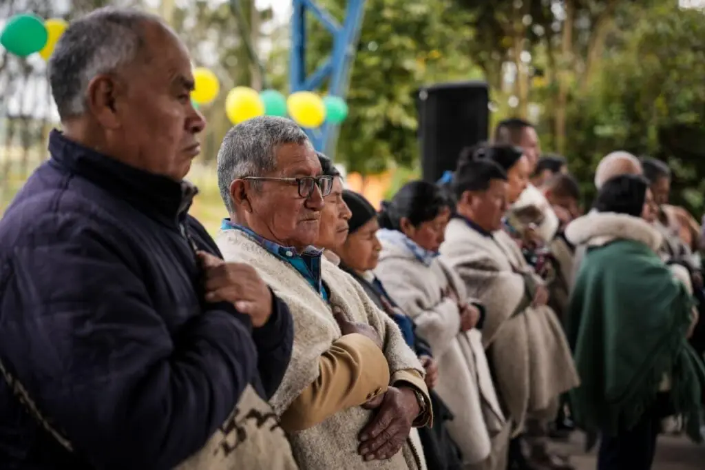Autoridades y mayores indígenas con vestimenta tradicional, de pie y con la mano derecha sobre el pecho durante un acto protocolario.