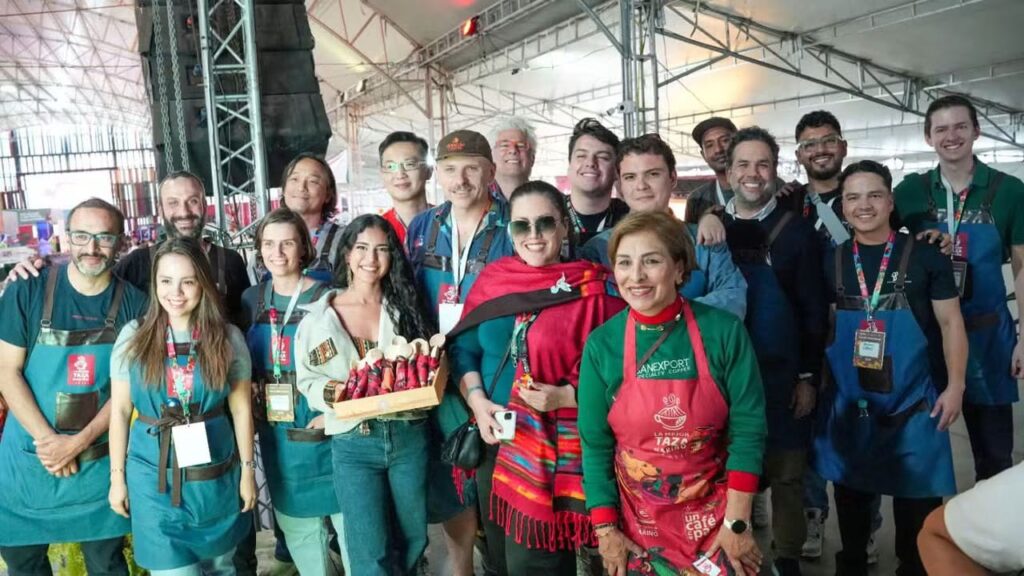 Gran grupo de asistentes, expositores y compradores internacionales posando sonrientes en el pabellón de la feria cafetera La Mejor Taza Nariño 2026.